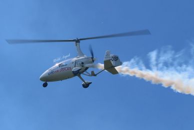 A small helicopter emitting white smoke against a blue sky.