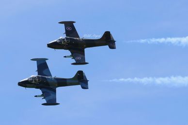 Two military jets flying closely with smoke trails against a clear blue sky.