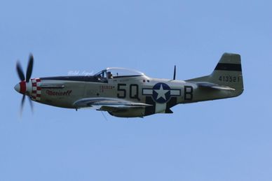A World War II-era P-51 Mustang aircraft flying in clear blue sky.
