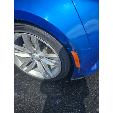 Close-up of a blue car's front wheel with water droplets.