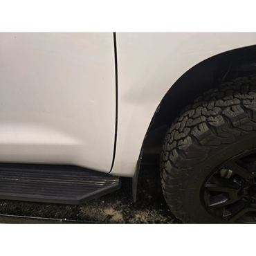 Close-up of a white vehicle's side panel, tire, and running board.