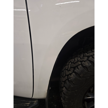 Close-up of a white vehicle's rear side and tire with rugged tread pattern.