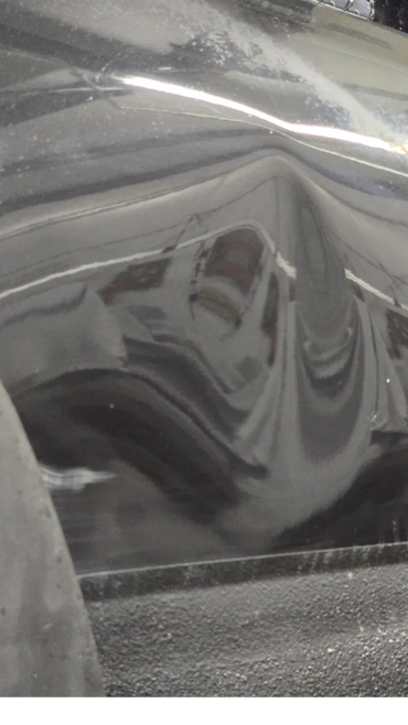 Black vehicle with a noticeable dent and scratches on the side panel.