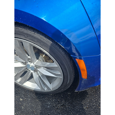 Blue car's front wheel and fender with water droplets.