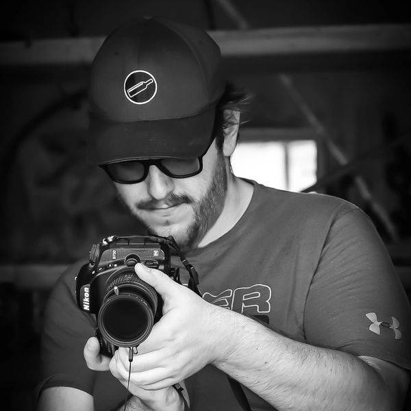 Man in cap and glasses holding a Nikon camera, focused on photography.