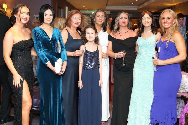 Eight women in elegant evening gowns posing together at a formal event.