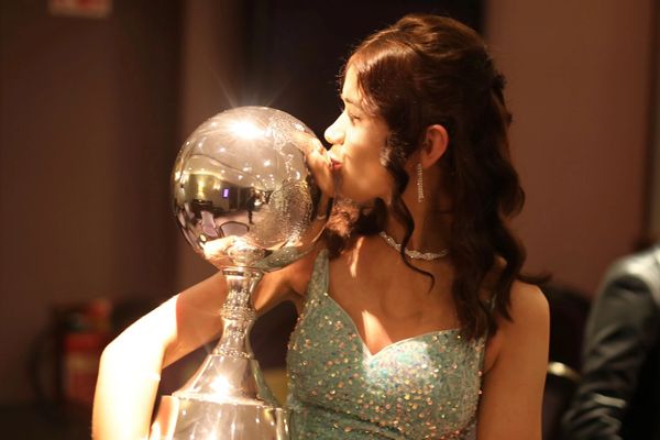 Woman in a sparkling dress kisses a large silver trophy in celebration.