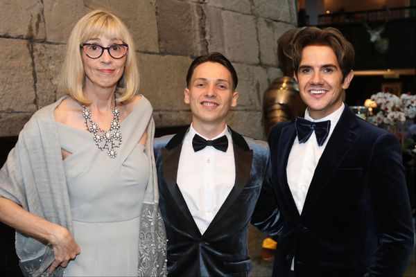 Three people dressed elegantly, smiling for a formal photo indoors.
