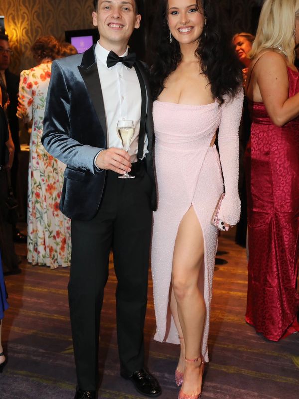 A smiling couple dressed elegantly at a formal event, posing for a photo.