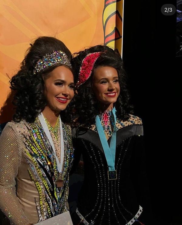 Two women in ornate costumes with medals smile for a photo.