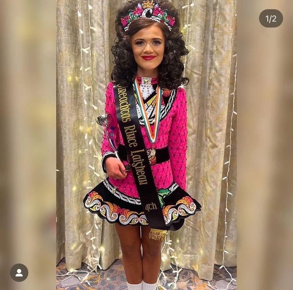 Young girl in vibrant Irish dance costume with crown and sash.