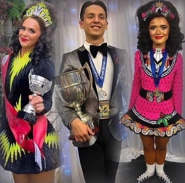 Three Irish dancers in colorful costumes holding trophies and medals, smiling proudly.