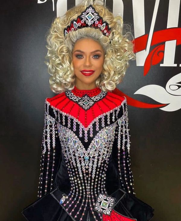 Woman in elaborate Irish dance costume with blonde curly hair and jeweled details.