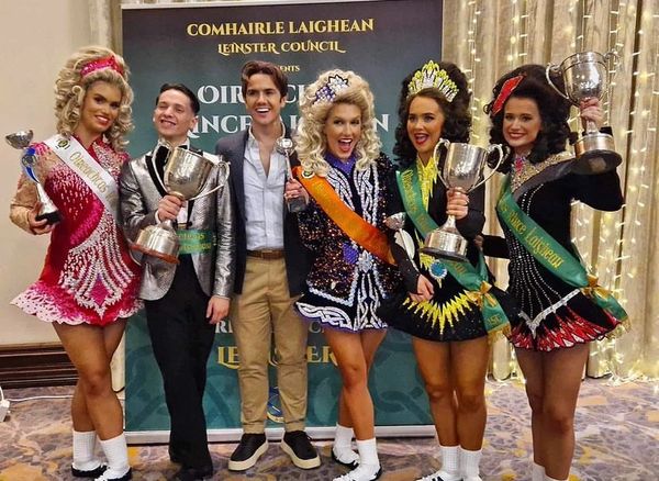 Group of Irish dancers and a man celebrating with trophies at a competition.