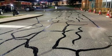Freshly sealed cracks on a parking lot at night with traffic cones nearby.
