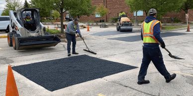 Workers paving a section of a parking lot with fresh asphalt.