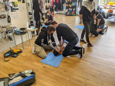 Two men practicing CPR on a dummy in a classroom.