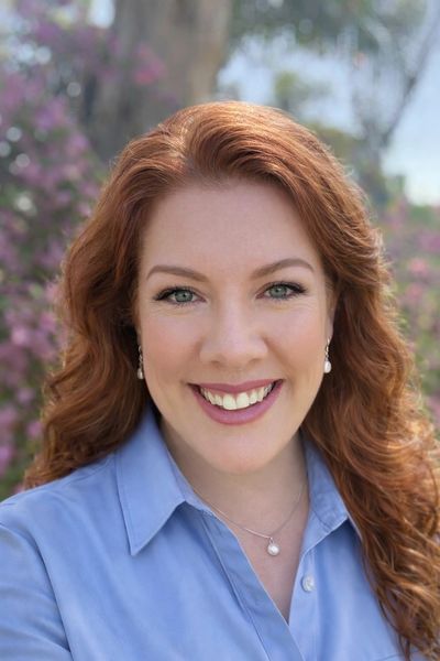Smiling woman with red hair and blue shirt outdoors.