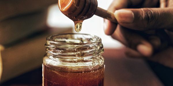 Hand dripping honey into a jar with a wooden honey dipper.