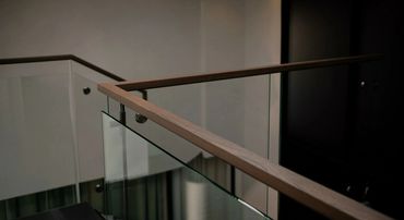 Modern staircase railing with glass panels and wooden handrails.