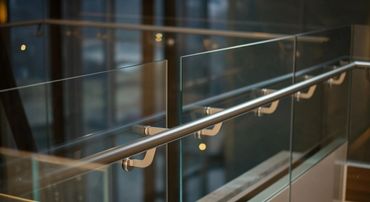 Modern glass railing with stainless steel handrail in a building.
