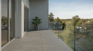 Modern balcony with glass railing and a potted plant overlooking suburban houses.