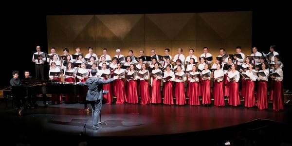 Large choir performing on stage with conductor and pianist.