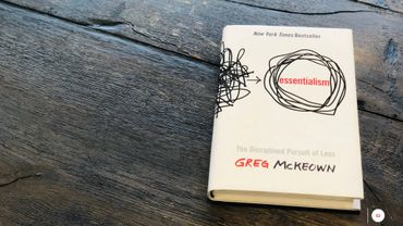 PowerPoint slide with a book laying on a wooden table named "Essentialism" by Greg McKeown