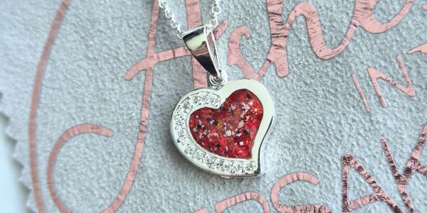 Heart-shaped silver pendant with red glitter and small stones.