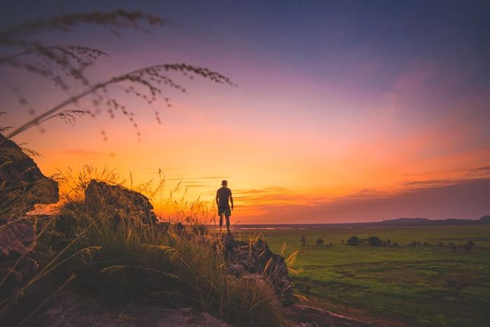 Silhouette of a person standing on rocks at sunset with a colorful sky.
