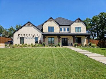 Modern two-story house with large green lawn and clear blue sky.