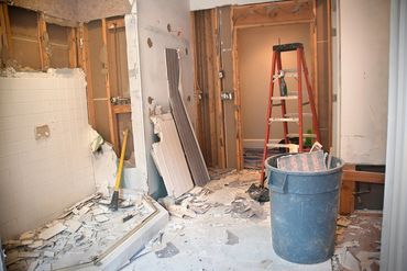 Bathroom under renovation with debris, a ladder, and a trash bin.