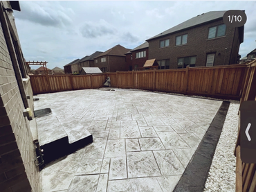 Backyard with patterned concrete patio and wooden fence under cloudy sky.
