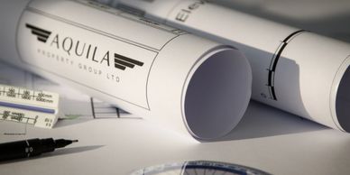 Rolled architectural plans labeled Aquila on a desk with a pen and ruler.
