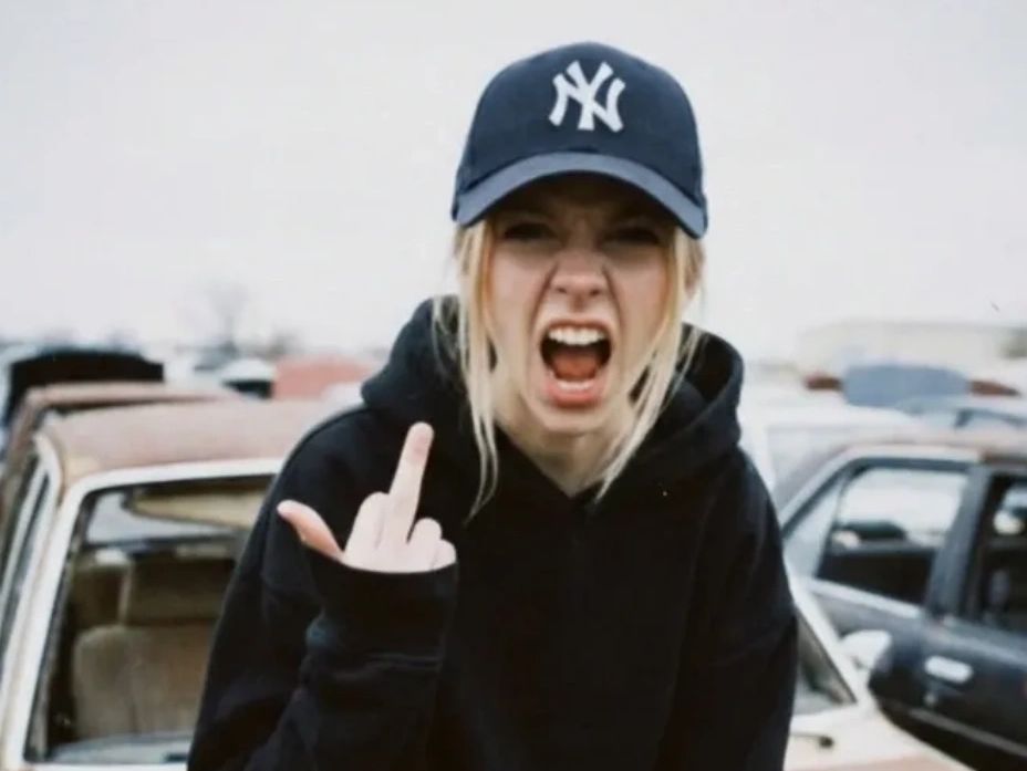 Young woman in a New York Yankees cap angrily showing middle finger.