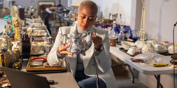 Woman inspecting a silver teapot in a room full of antiques and collectibles.