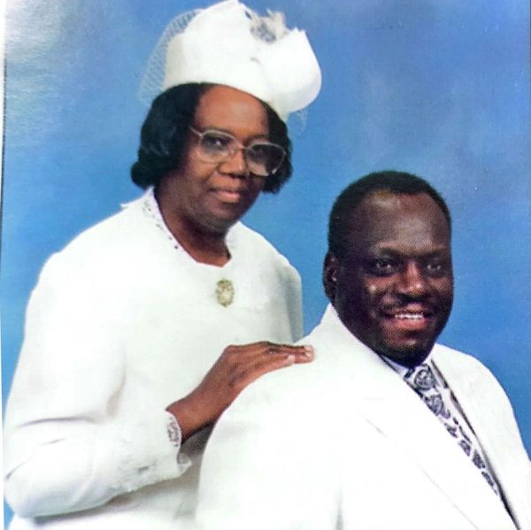 A formally dressed couple poses against a blue backdrop.