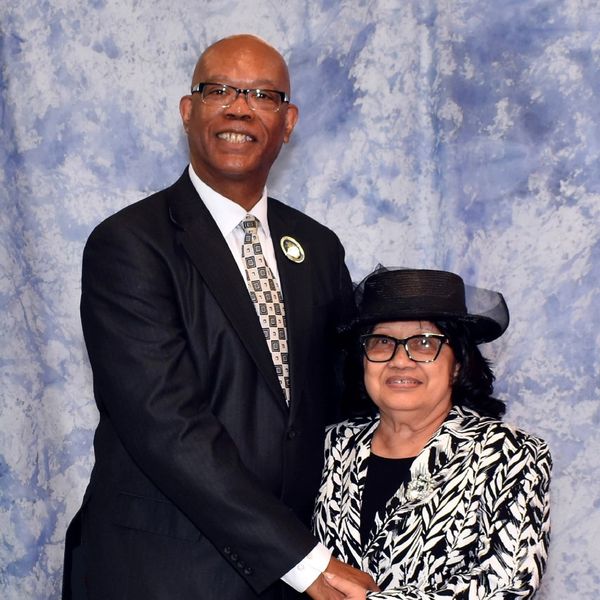 A man and a woman dressed formally, posing together against a blue backdrop.