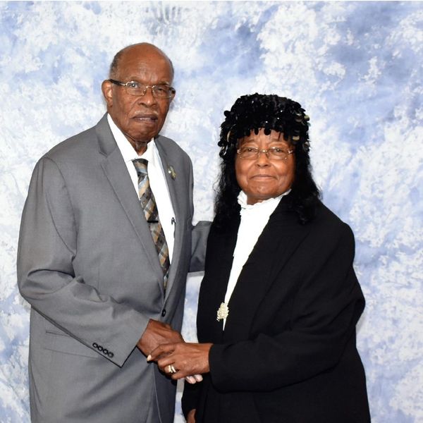 Elderly couple dressed formally, holding hands and posing together.