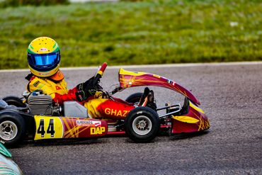 Go-kart racer in yellow and red gear driving on a track.