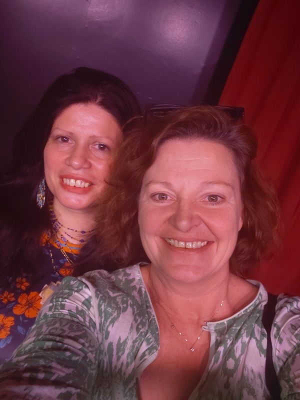 Two women smiling for a selfie indoors with colorful clothing.