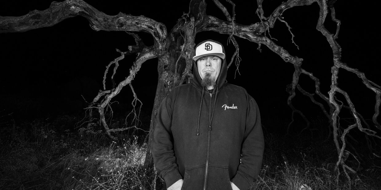 Man in hoodie standing in front of a twisted tree at night.