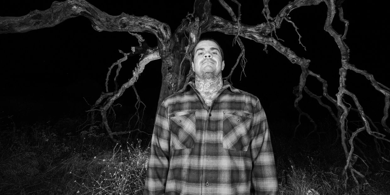 Man standing in front of a bare, eerie tree at night.