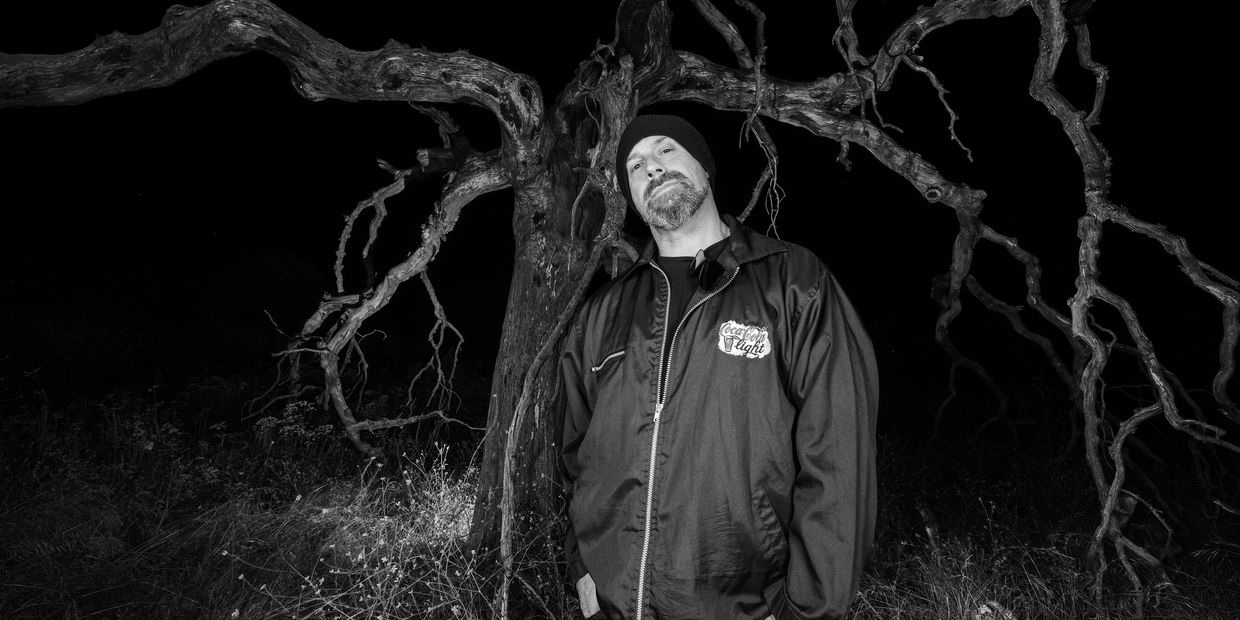 Man posing in front of a gnarled tree at night.