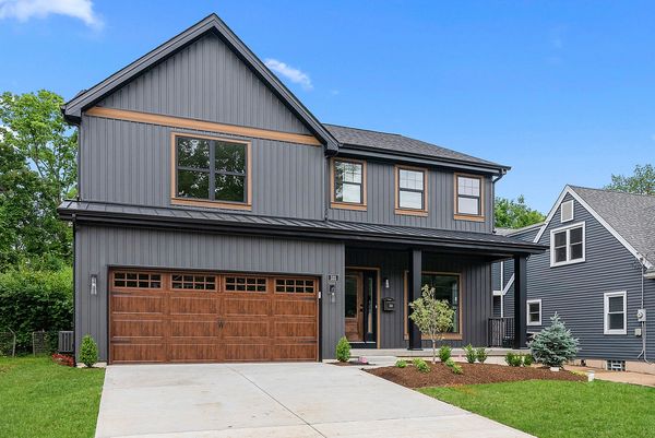 Modern two-story gray house with wooden garage door and fresh landscaping.