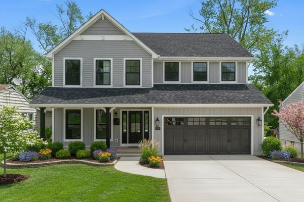 Two-story gray house with black garage doors and well-manicured lawn.