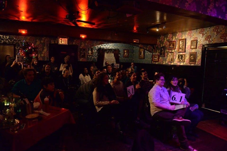 A crowd of spectators and judges cheer on a poet performance with score cards showing.