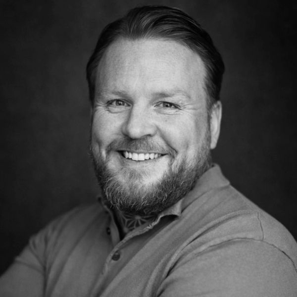 Smiling man with beard and tattooed arm in black and white portrait.