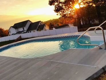 Sunset over a backyard pool with houses and trees in the background.
