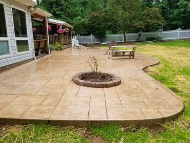 Spacious backyard patio with a built-in fire pit and surrounding greenery.